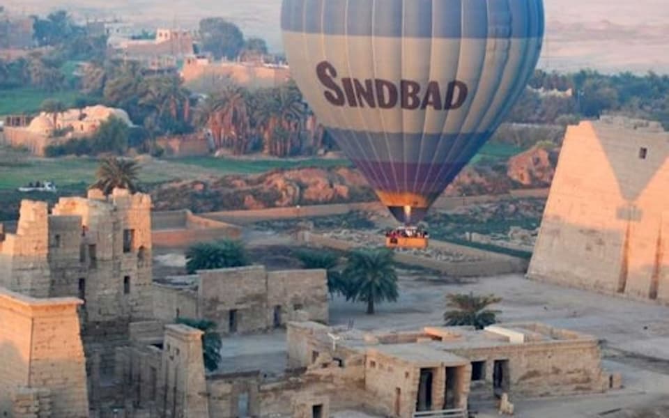Sindbad hot air balloon drifting over ancient temple ruins at sunrise in Luxor, Egypt