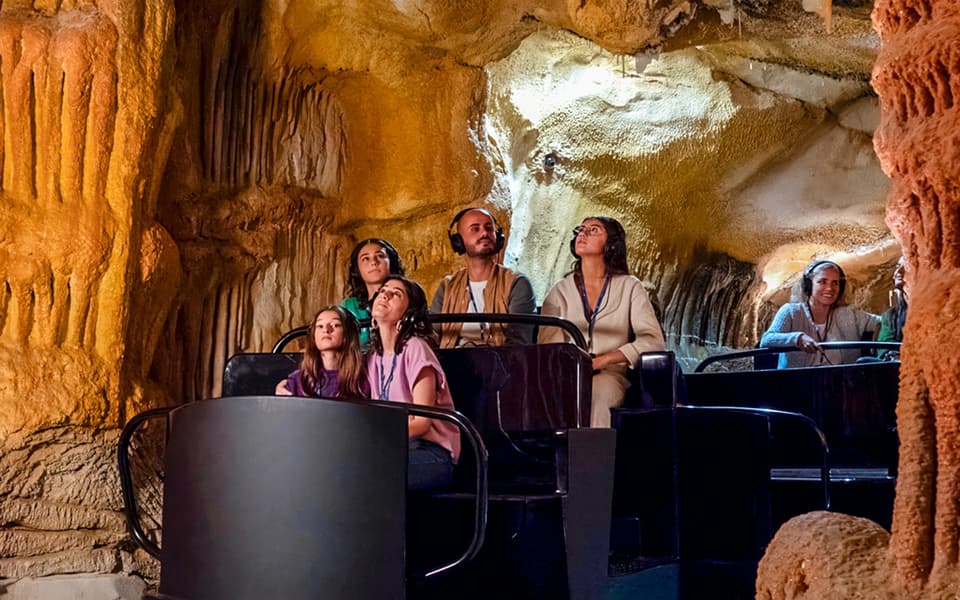 Visitors on a ride gazing up at golden rock formations inside an immersive cave attraction in Marseille