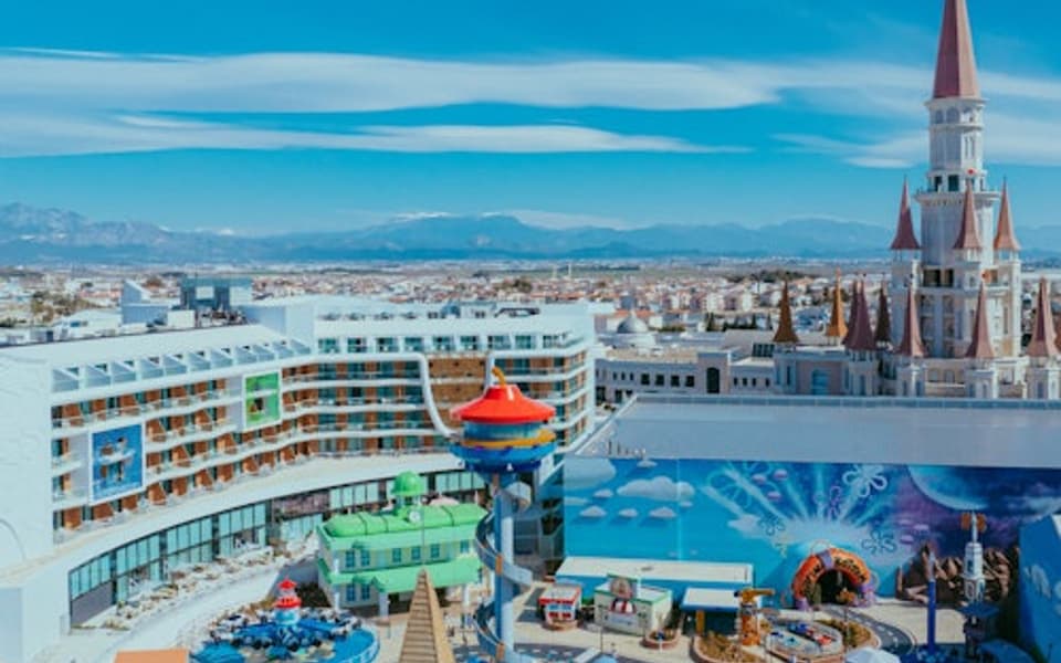 Colourful theme park with a fairytale castle tower and mountains behind in Antalya