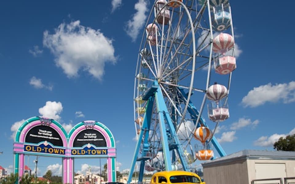 Old Town Kissimmee entrance arch and Ferris wheel with a yellow classic car under a blue sky