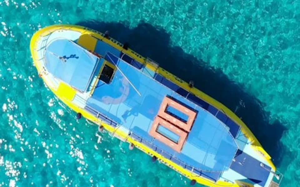 Aerial view of a yellow and blue tour boat with swimmers in turquoise sea off Rhodes