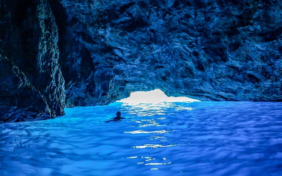 Swimmer in the glowing blue water of a sea cave near Dubrovnik, Croatia