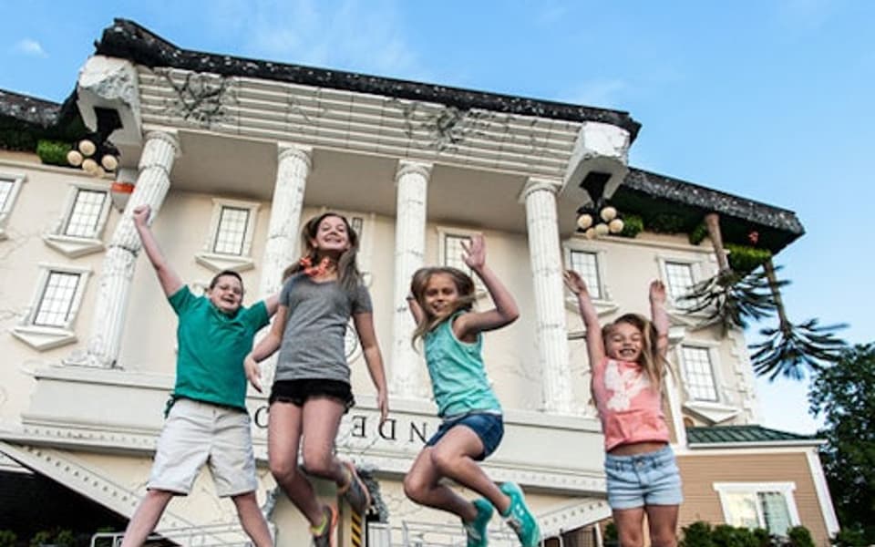 Four children jumping outside the upside-down house attraction in Pigeon Forge, Smoky Mountains