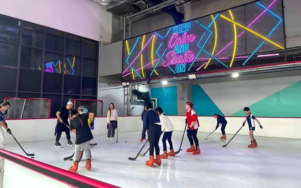 People skating on an indoor ice rink in Kuala Lumpur beneath a neon Keep Calm and Skate On sign