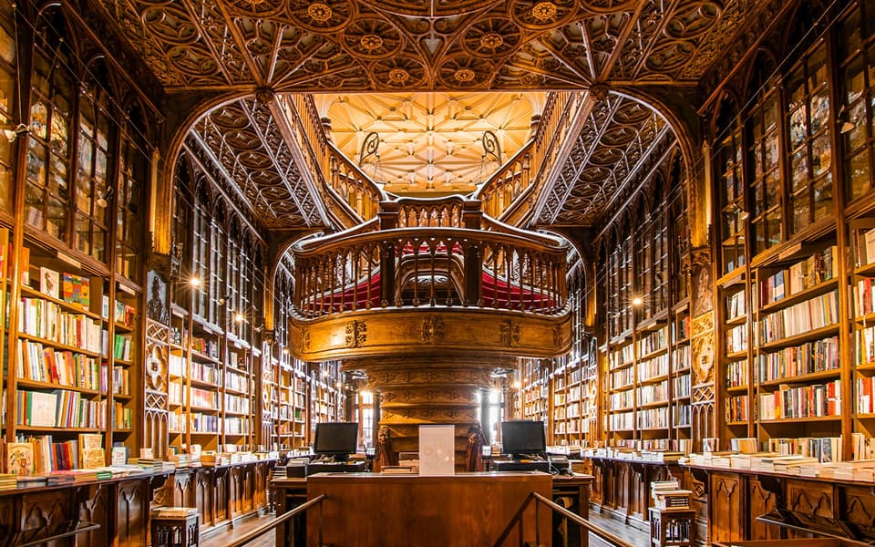 Carved wood staircase and stained-glass ceiling inside Livraria Lello bookshop in Porto