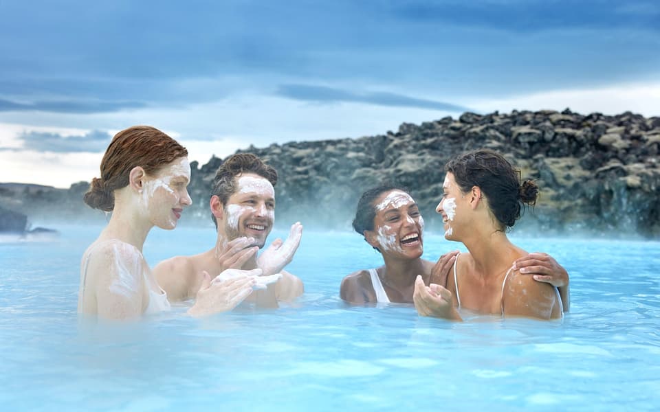 Four friends relaxing with silica face masks in a steaming geothermal spa among Iceland's lava rocks