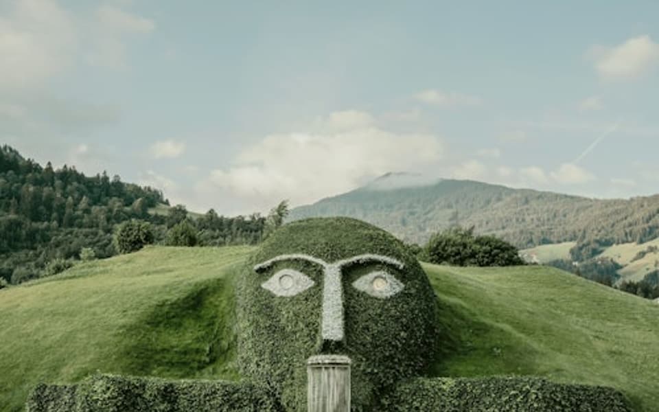 Swarovski Crystal Worlds giant grass-covered face fountain below Alpine peaks near Innsbruck